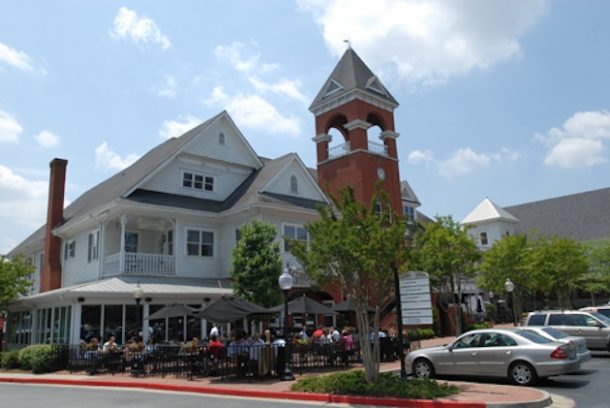 Outdoor dining at a charming corner restaurant on a sunny day, with a classic clock tower rising in the background.
