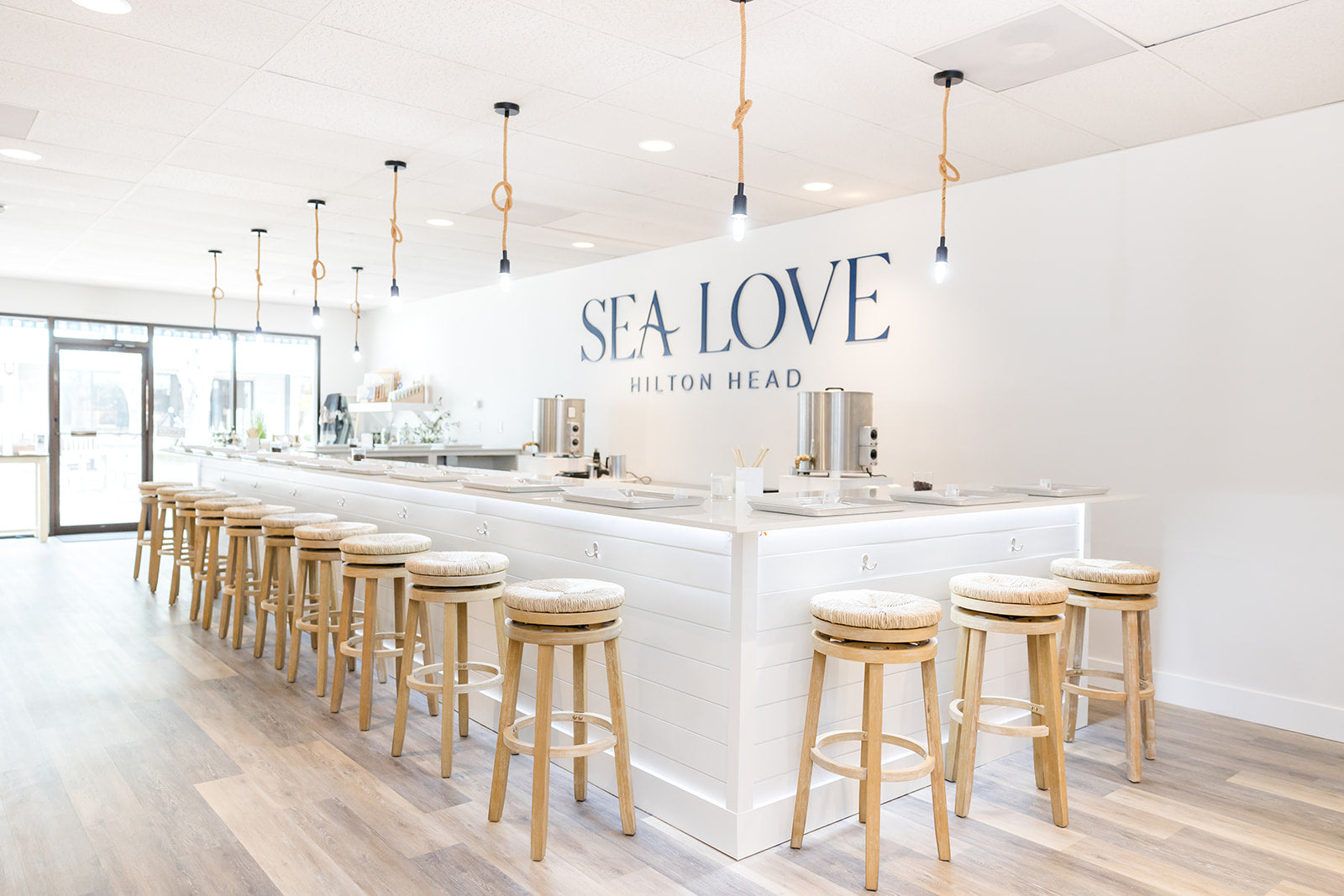 Bright and modern seaside-themed candle bar interior with clean white aesthetics and wooden stools.