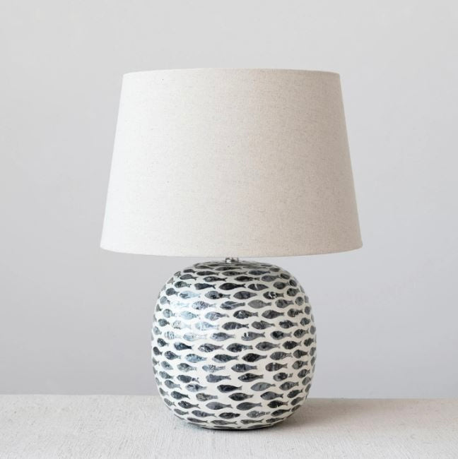 A ceramic table lamp with a round base featuring a black and white tear-shaped pattern, topped with a plain off-white lampshade.